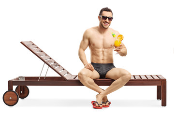 Young attractive man sitting on a sunbed and holding a cocktail