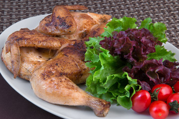 Roasted chicken on a white oval dish with fresh tomatoes and lettuce