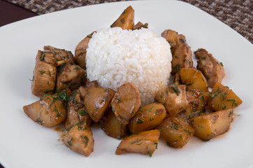 Stewed potatoes with slices of beef in a spicy sauce on a white plate with a cut of white crisp rice