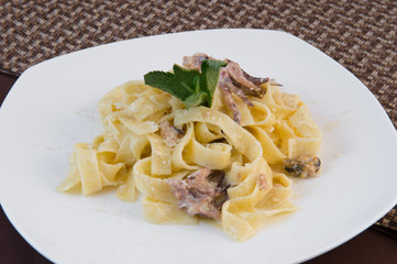 Wide white octopus noodles decorated with a sprig of mint on a large white plate on a brown background
