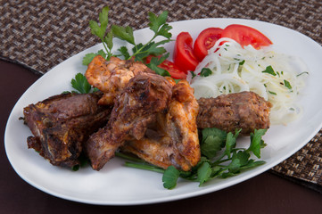 Assorted meat. Lamb ribs with fat, chicken slices and wings, cradles on a large white dish with slices of tomato, parsley and onion rings