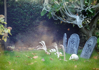 Halloween decorations of traditional english garden. Creepy skeletons awake from theirs graves. 