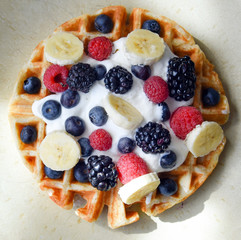 Perfect belgian waffle with bananas, strawberries, blackberries, blueberries and whipped cream from above