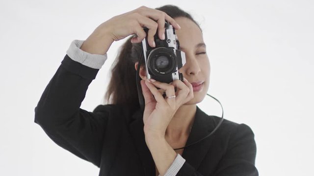 Young appealing brunette in black jacket holds picture camera takes a few photos of viewer and lowers device to access results. 4K footage.