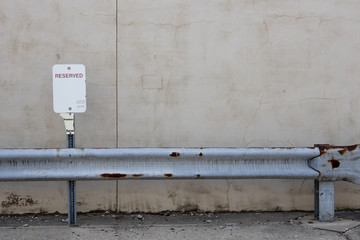 Reserved blank parking sign with metal rusting guard rail in front and stucco wall behind
