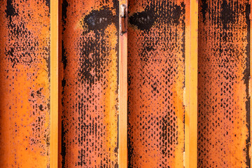 Rusted yellow and orange faded paint over metal textured sheets welded together