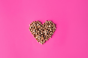 Fototapeta premium Top view of the heart with uncooked buckwheat isolated on the pink magenta background. gluten free ancient grain for healthy diet, selective focus.