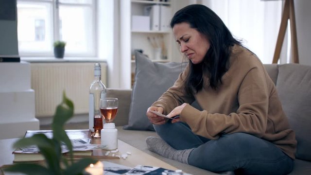 Depressed woman with alcohol indoors, tearing photograph.