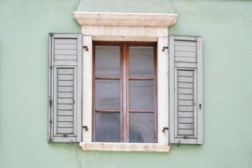 Fototapeta na wymiar Italian window on the green color wall facade with open wooden green shutters