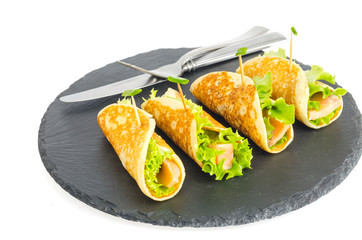 Pancake rolls with fish and lettuce. Salmon bread roll with cheese. On black stone plate.