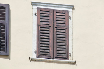 Fototapeta na wymiar Italian window on the bright wall facade with closed wooden shabby brown color shutters