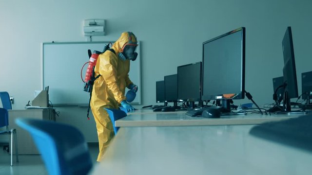 Covid19, coronavirus concept. Worker in hazmat sanitizes desks with computers.