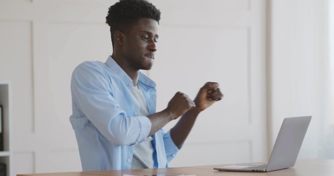 Happy emotional african american guy dancing near laptop