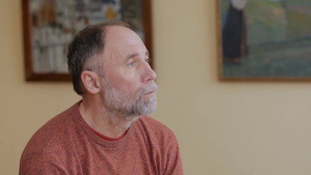 An elderly man looks thoughtfully at art objects sitting on a bench in a Museum
