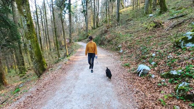 Woman in casual clothes walking with small black dog in nature, footage with action camera