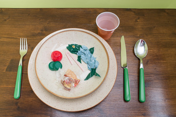 Plastic pollution comes to our tables. Plastic and microplastics pollute the sea and We eat fish wit that have absorbed plastic. Dish with fish and side dishes made of plastic. Isolated on a table.