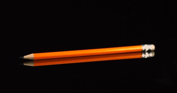 Yellow school pencil falling in slow motion. Pencil drop isolated on a black background.