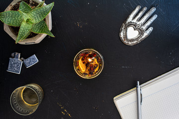 Overhead view of a candle with a lighter, a heart shaped Hindu ornament, a paper personal diary, and an aloe plant on a black vintage desk