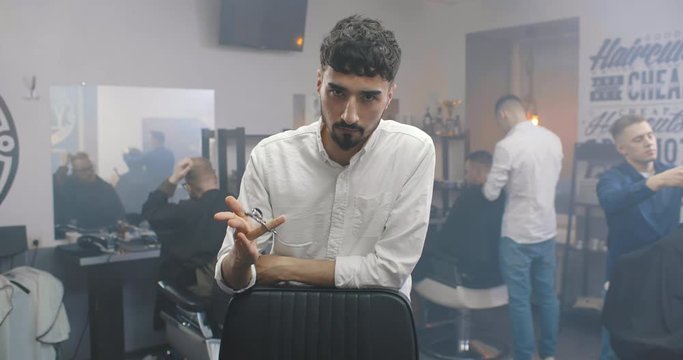 Bearded professional barber with scissors looking at camera
