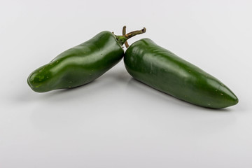 Two jalapeño chili peppers lay on a white table against a white background. Peppers are great ingredients for cooking Latin food.