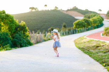 Portrait of adorable little girl with long blonde hair outdoor near tea plantation. Beautiful child. Happy smiling kid on sunny summer day, childhood day, education concept