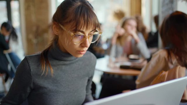 beautiful female developer or student in yeyglasses working, studying by laptop in cafe. freelance, remote work, online education, self employed