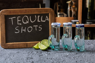 Tequila shots served in traditional mexican glasses, with chalkboard sign and limes