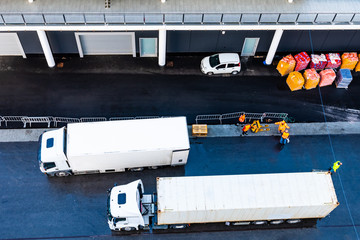 White 10 (ten) wheeler freight truck parked next to 18 (eighteen) wheeler delivery trailer on asphalt road inside shipping/ shipment delivery port.