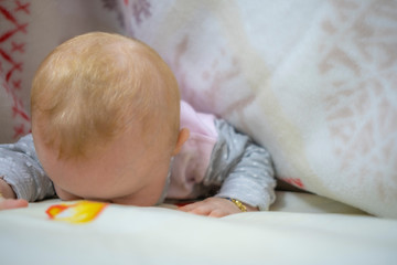 Close-up portrait of little cute baby girl standing under the blanket on bed and looking at camera