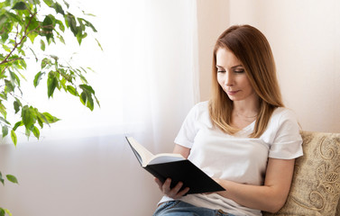Fototapeta premium Happy young woman reading storybook on couch at home