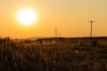 Fototapeta na wymiar Blazing hot sun over a dry grass western desert with telephone poles leading into the distance