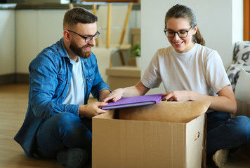 Happy couple looking at photo album while unpacking stuff after relocation to new flat