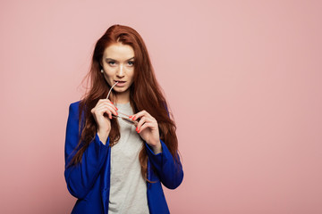 A redhead girl is on the pink background. A wily redhead girl is on the pink background. A tricky girl is on the pink background. A mysterious woman with glasses