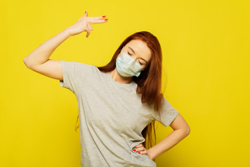 A readhead girl is in protective mask on the yellow background. A girl is shooting. A woman want to be save and healthy. Advertising of safety mask. Virus can kill you