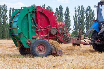 tractor makes big straw roll on yellow field at summer day
