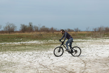Obraz premium Sports brutal bearded guy on a modern mountain bike. A cyclist in a salt deserted place by the lake.