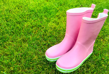 Pink rubber boots stand on green grass.