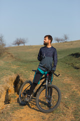 Cyclist in shorts and jersey on a modern carbon hardtail bike with an air suspension fork standing on a cliff against the background of fresh green spring forest