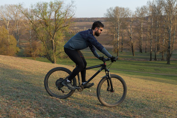 Obraz premium Cyclist in shorts and jersey on a modern carbon hardtail bike with an air suspension fork standing on a cliff against the background of fresh green spring forest