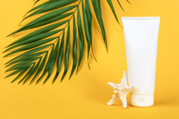White blank cosmetic tube with sunscreen, suncream for face or body, starfish and green brunch palm on yellow background. Concept skin care in summer holiday Mockup Front view Copy space