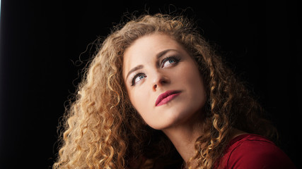 Close-up portrait of a curly hair girl looking up over black background. Blond model in the studio, mysterious look blue eyes. European appearance