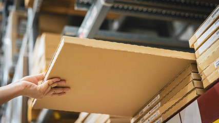 Cardboard box package with blur hand of Asian shopper woman picking product from shelf in warehouse. customer shopping lifestyle in department store or purchasing factory good concepts.