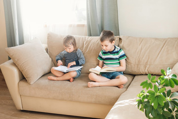 Children reading a book at home on sofa. Distance learning education. Digital detox.