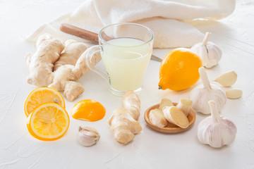 Ginger, garlic, lemon, dried medical chamomile in a jar and ginger tea - a means to protect against viral infections and colds on a light wooden table.
