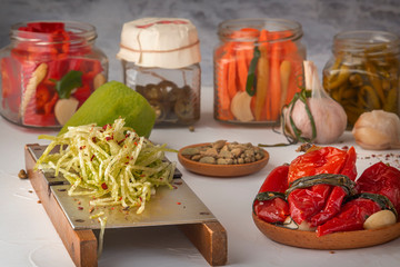 Radish grated on a hand grater on the background of differentiated products - pepper, garlic, carrots on a light wooden table