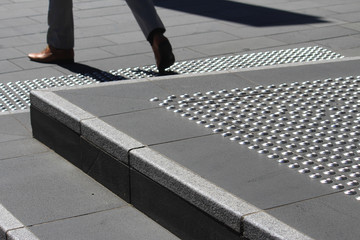 Man legs stepping down from steps. The steps have stainless steel tactile indicator studs that have...
