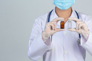 Beautiful young doctor is wearing mask while holding alcohol on gray background.