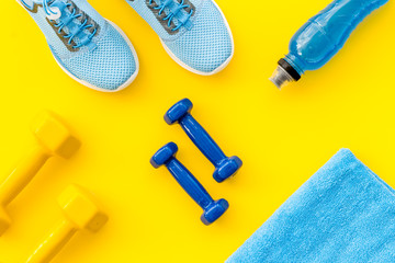 Obraz na płótnie Canvas Athletics flat-lay with dumbbells, towel, sneakers on yellow background top-down