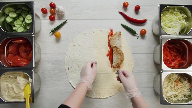 Top view of chef hands in white gloves puts beef cutlet on doner kebab shawarma in pita or lavash. Shawarma with chicken cutlet, pappers, cheese and vegetable