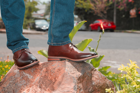 Outdoor photo of brogue shoes with blue socks against a rocky background, standing on a rocky boulder.